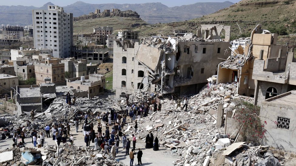 Yemenis stand amid the remains of a block of flats destroyed in an air strike in Sanaa, Yemen (26 August 2017)