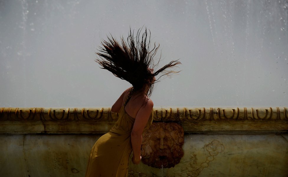 A woman refreshes herself in a fountain at Plaza de Espana, on a hot summer day in Sevilla