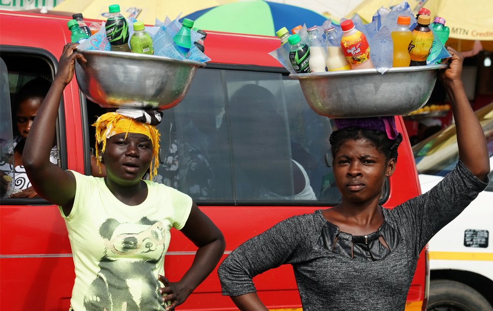 Women carrying drinks on their heads watch as the motorcade that carries the media covering U.S. first lady Melania Trump passes in Accra, Ghana, October 2, 2018