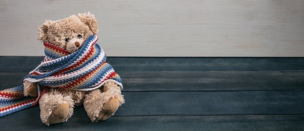 Cute teddy bear with colorful scarf sitting on blue wooden background