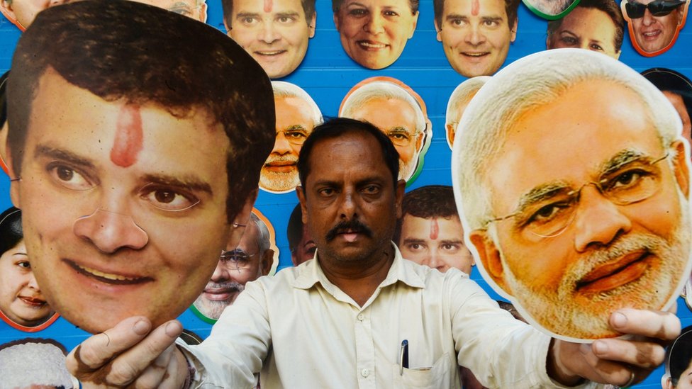 A shopkeeper poses with masks of Congress party leader Rahul Gandhi and Indian Prime Minister Narendra Modi