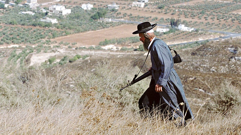 An armed Jewish settler walks in a field in the occupied West Bank