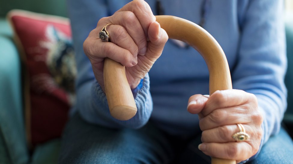 An elderly woman's hand holds a walking stick