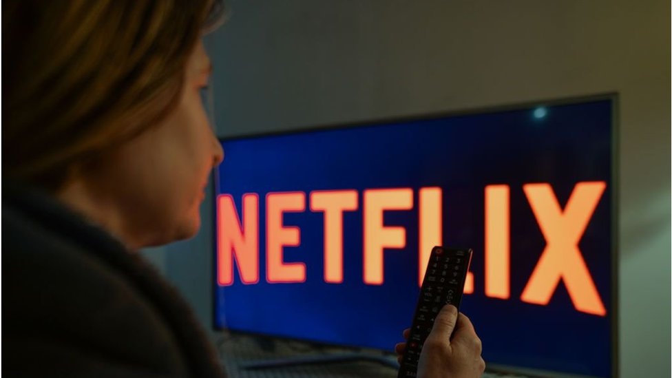A woman sit in front of a TV with the Netflix logo on the screen