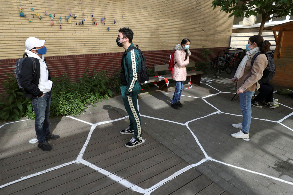 Students stand separately in designated hexagon shapes on the floor