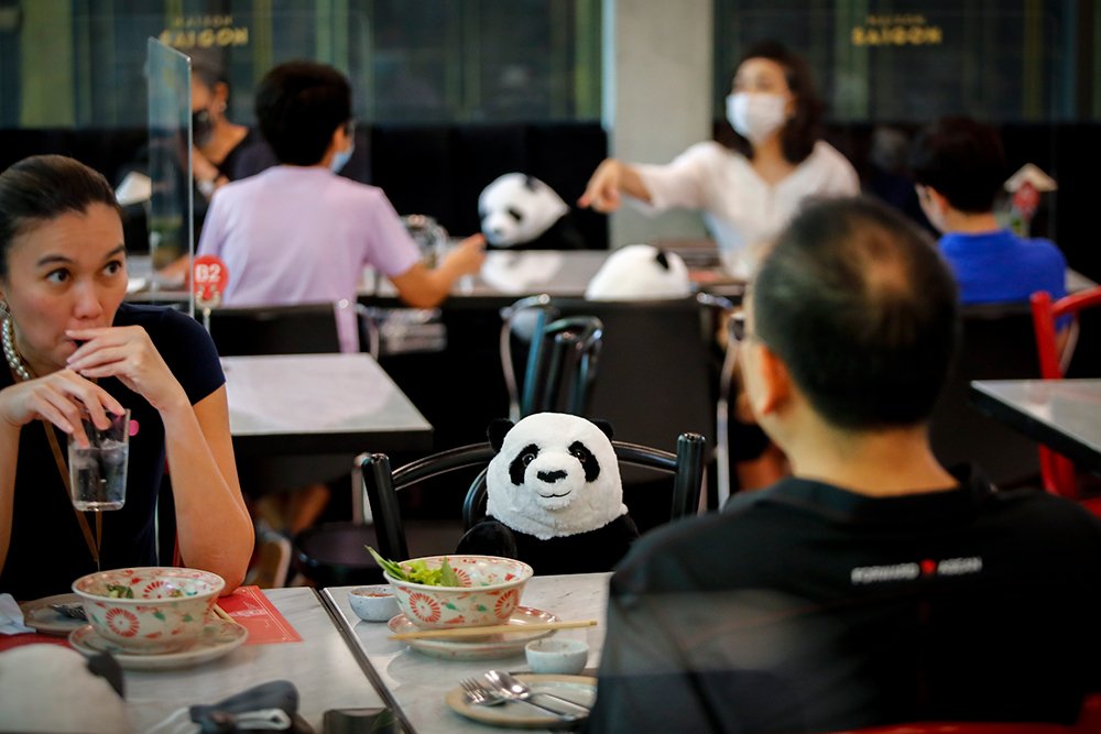A stuffed panda is seen on a chair next to diners in a restaurant