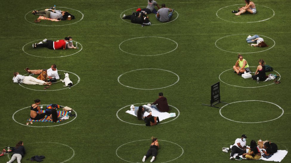 People sit in circles meant to encourage social distancing in Domino Park along the East River on May 18, 2020 in the Williamsburg neighborhood of the Brooklyn borough in New York City