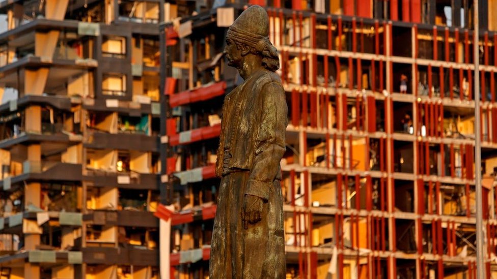 The statue of the Lebanese Emigrant stands intact in front of damaged buildings