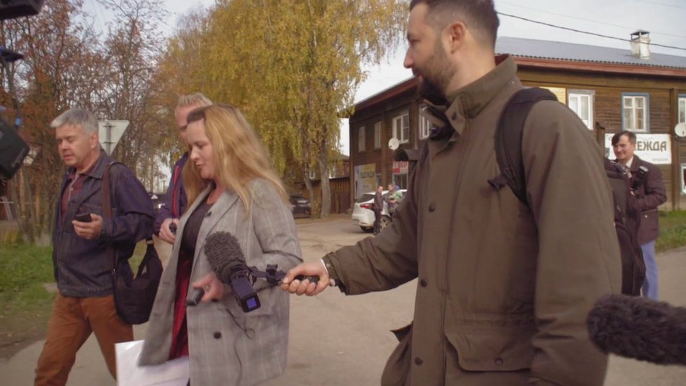 The BBC's Petr Kozlov holds a microphone towards Marina Udgodskaya with other journalists around