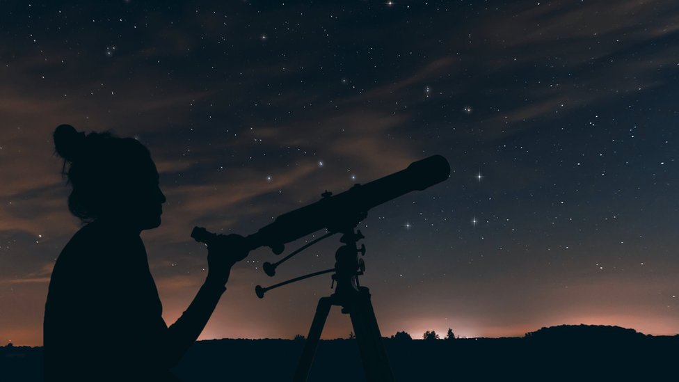 A woman looking at the night sky with a telescope