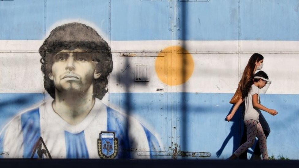 Two people walk past a mural of Maradona