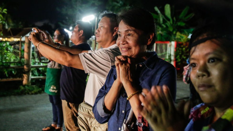 An onlooker clasps her hands as she cheers on ambulance taking the children