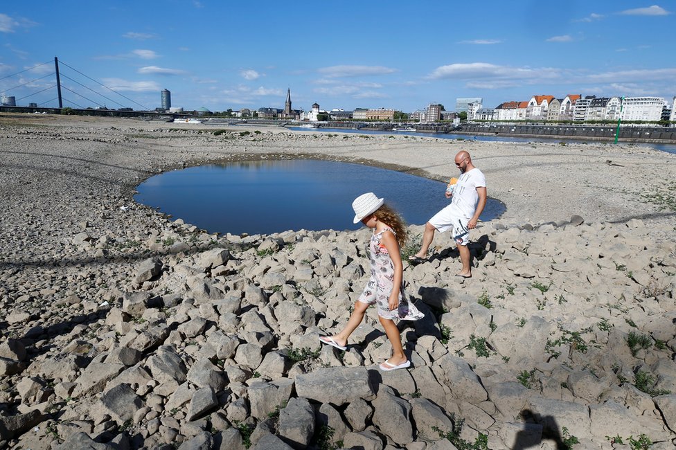 A family walks next to a puddle in the partially dried riverbed of Rhine, in front of the skyline of Dusseldorf, Germany