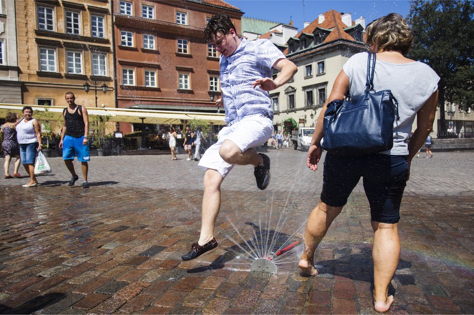 People cool themselves with sprinklers during the heat wave in Warsaw