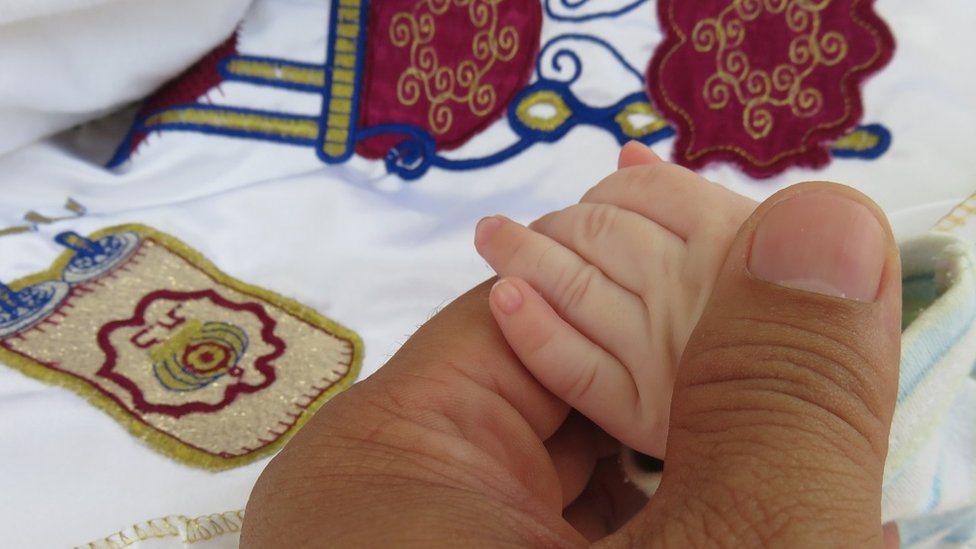 A father holds a baby's hand before circumcision