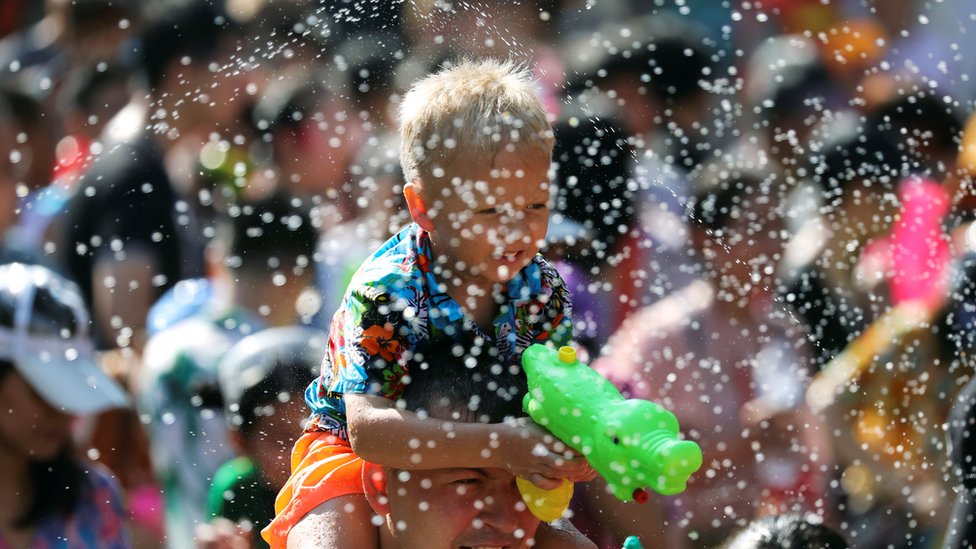 A boy sits on a person's shoulder while holding a water gun