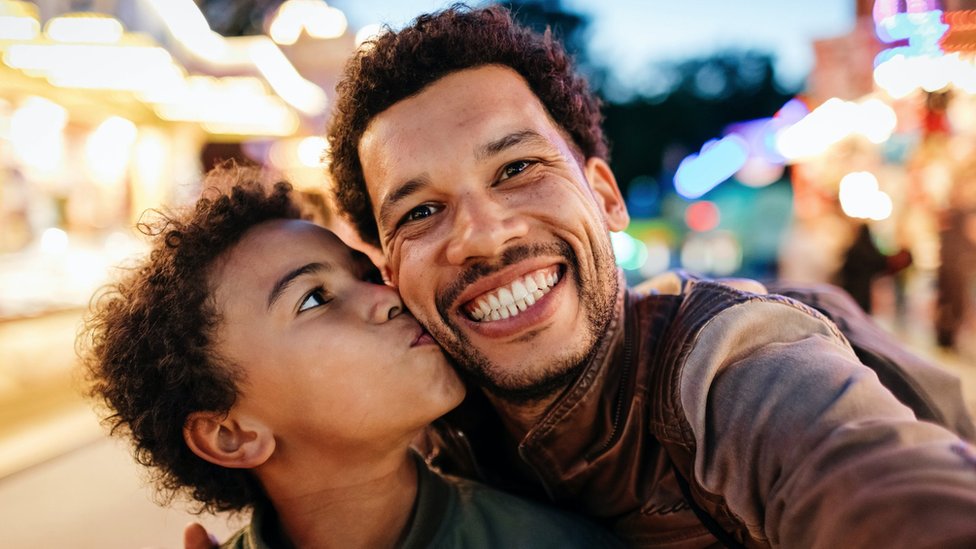 A boy kisses his father's cheek as they pose for a selfie