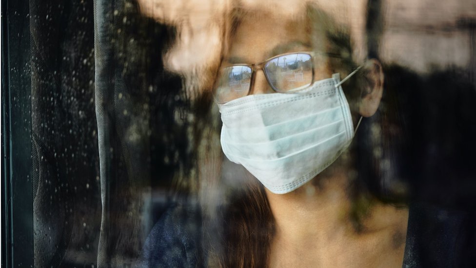 Woman looking through a wet window during lockdown because of Covid-19 - stock photo