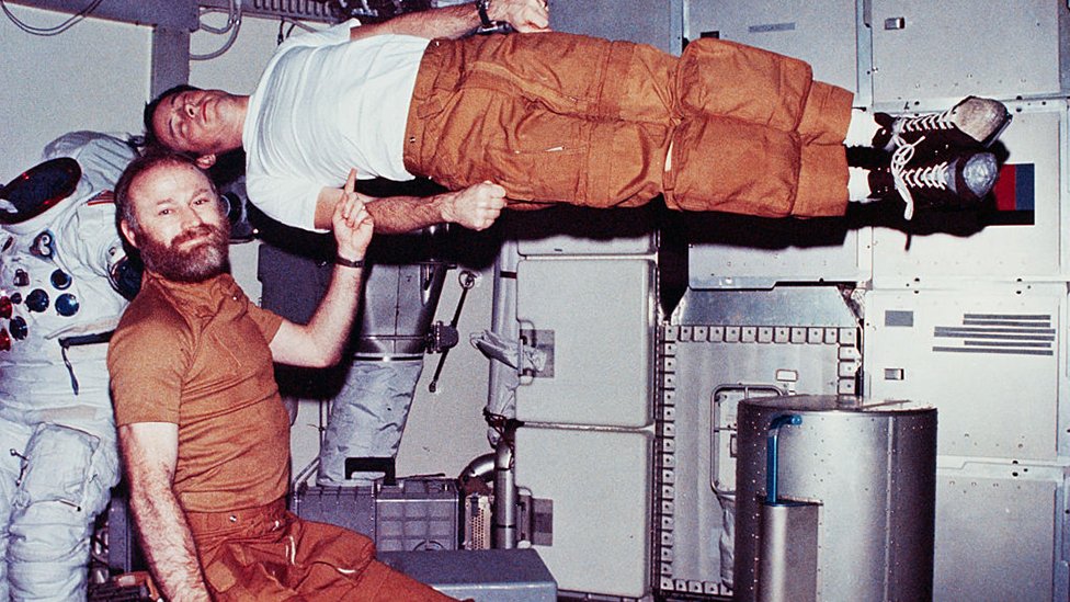 Jerry Carr demonstrates weightlessness by pretending to hold up Ed Gibson with one finger