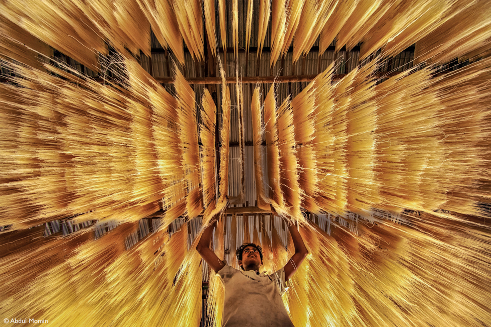Man reaching up to rice noodles that are hanging above him
