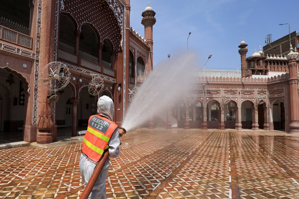 A worker sprays disinfectant from a hose at the exterior of a mosque