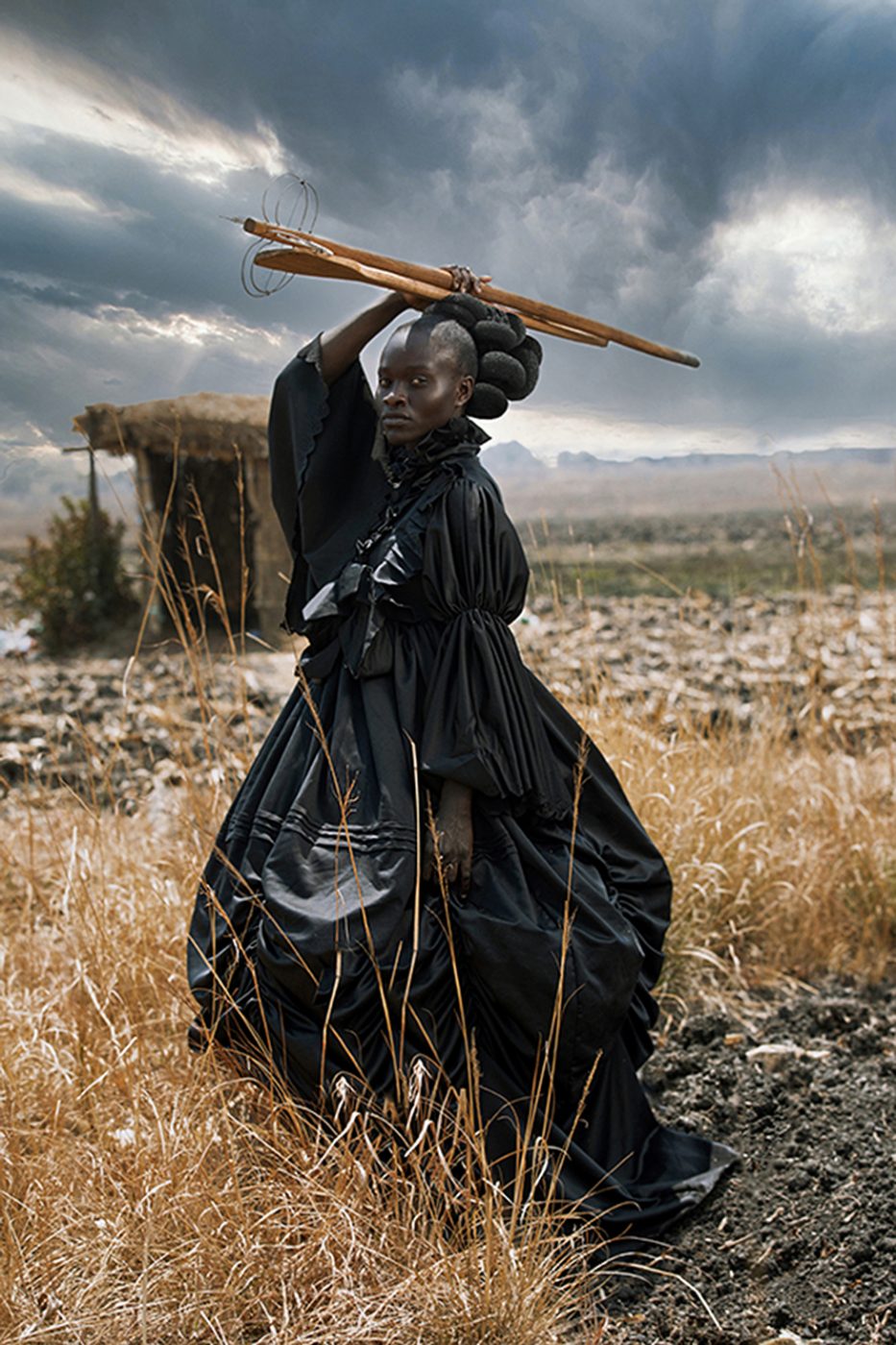 Portrait of a young woman dressed in a Victorian dress and holding traditional Shona cooking utensils