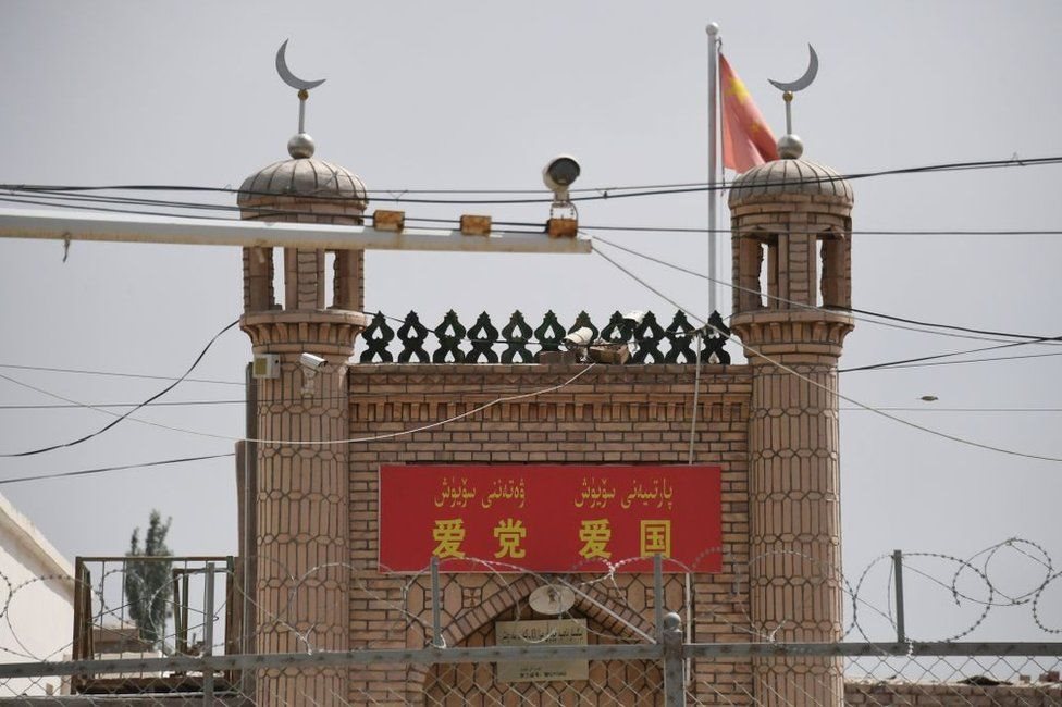 A closed down mosque near Kashgar, with barbed wire and a surveillance camera in the foreground