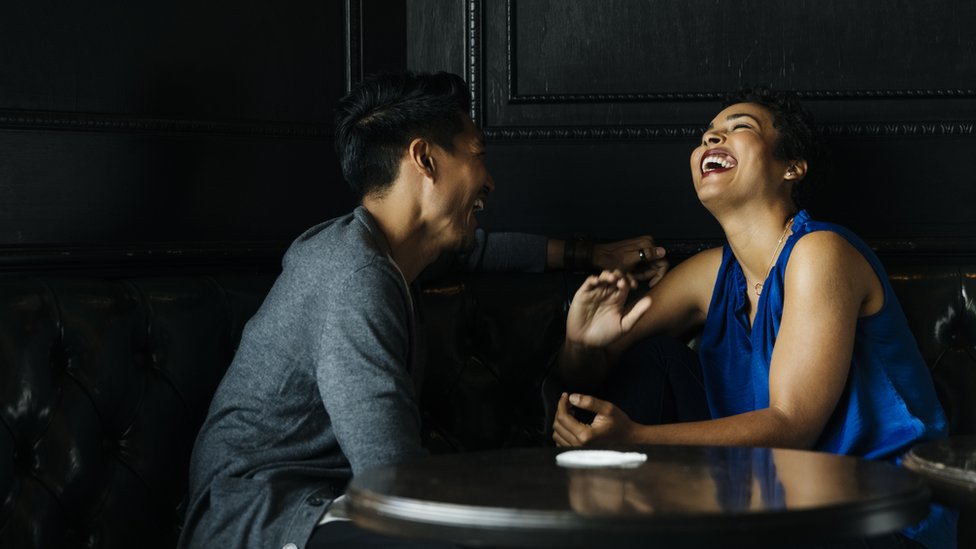 A man and a woman sit at a table talking and laughing.