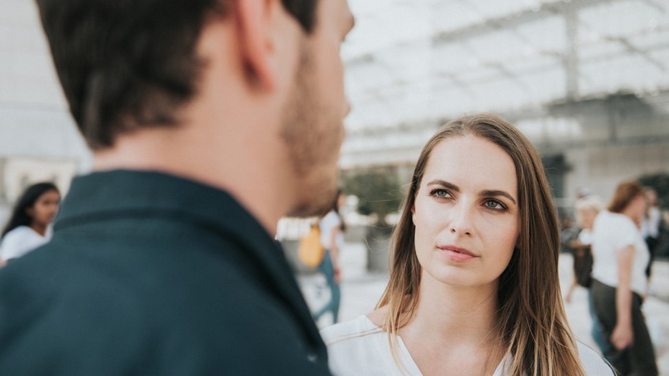 A woman listens to a man speaking with a slightly sceptical face