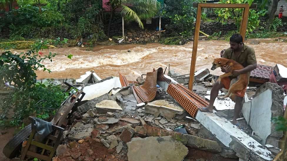 A resident carries a dog amid debris of his damaged house after flash floods caused by heavy rains at Thodupuzha in India's Kerala state, 16 October 2021