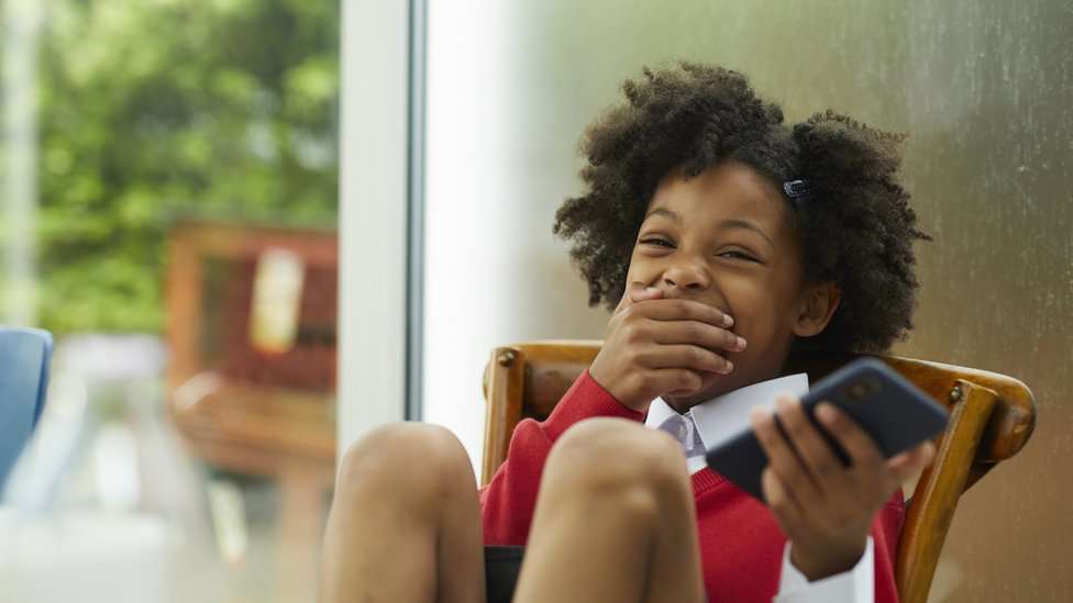 A girl sitting at a kitchen table at family home, wearing school uniform at breakfast in the morning. She is playing on a smartphone