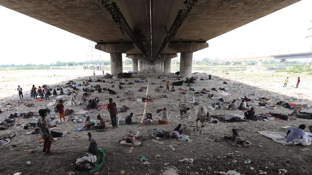 Crowd of people under a bridge sheltering from the heat.