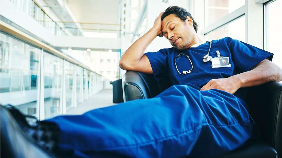 A tired doctor sleeps in a hospital armchair