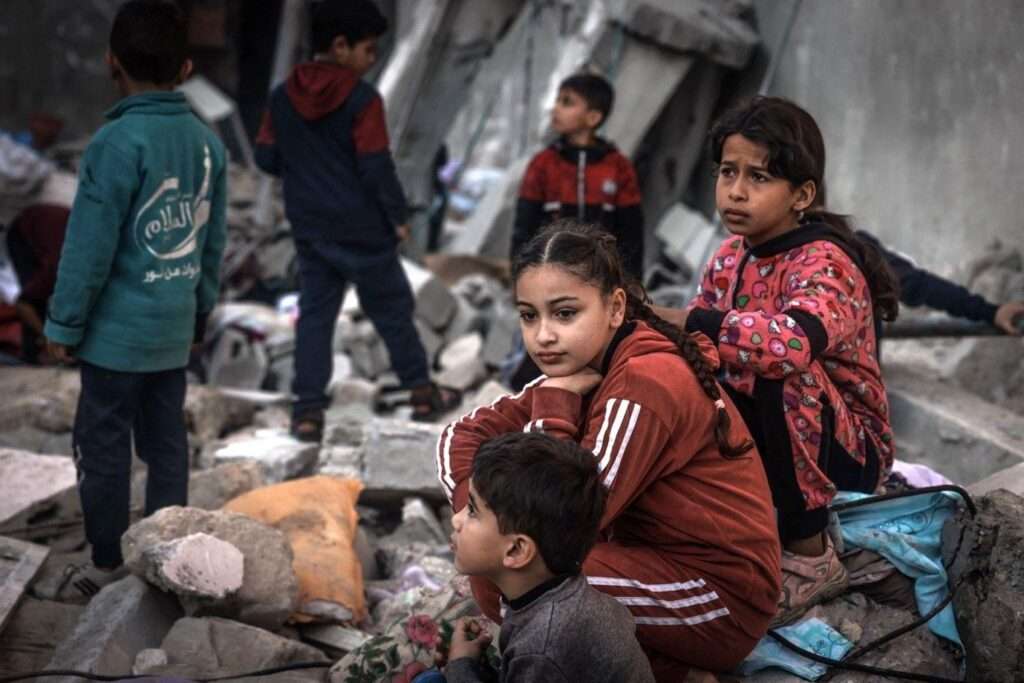 29 دسمبر 2023 کو جنوبی غزہ کی پٹی میں رفح میں اسرائیلی بمباری کے بعد تباہ شدہ عمارتوں کے ملبے کے درمیان بچے بیٹھے ہیں