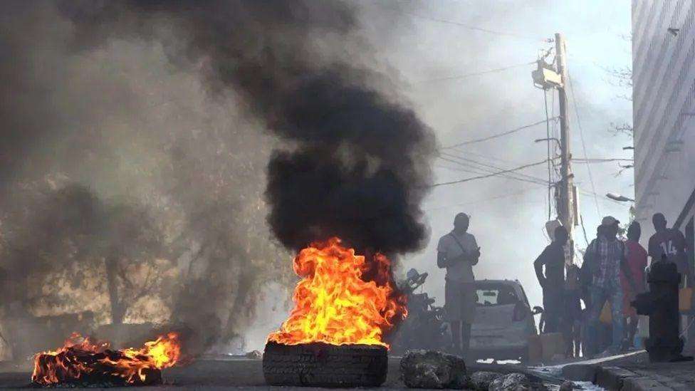 Tyres burning in the street with people standing around nearby
