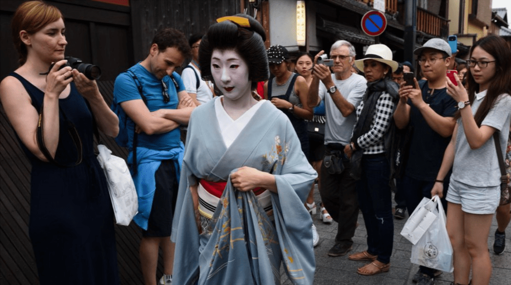 Tourists take photographs of a geiko walking through the Gion area of Kyoto, Japan, on Thursday, May 28, 2015.